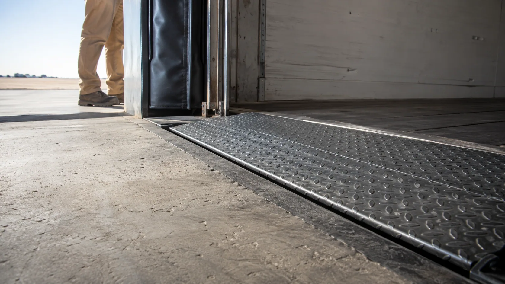 Illustrative low-angle view across a warehouse dock leveler toward an empty trailer.